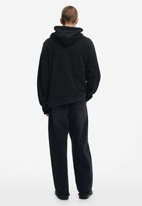 Svart överdimensionerad huva sweatshirt med en texturerad design, parat med löst sittande svarta denimbyxor och svarta skor.