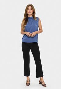 Top senza maniche blu con scollatura arricciata, abbinato a pantaloni neri slim-fit e décolleté con stampa animale. Tessuto liscio con una vestibilità comoda.