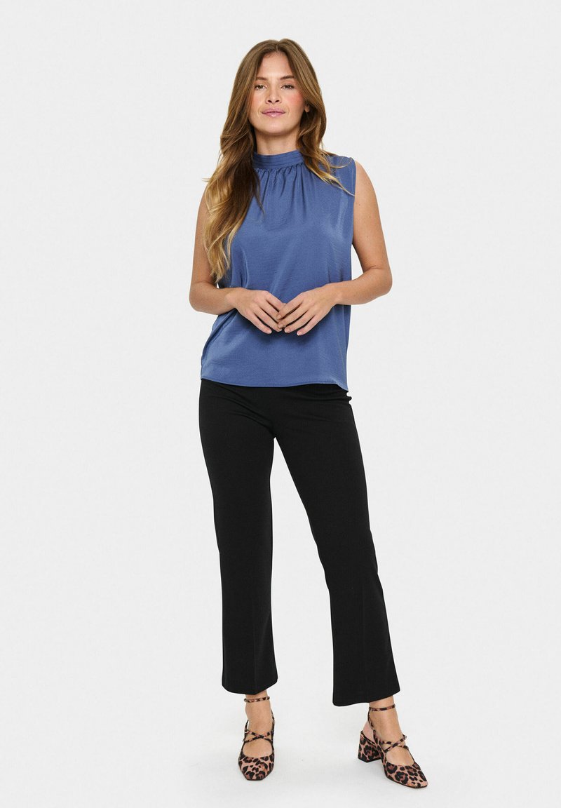Top senza maniche blu con scollatura arricciata, abbinato a pantaloni neri slim-fit e décolleté con stampa animale. Tessuto liscio con una vestibilità comoda.