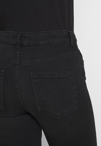 Jeans de mezclilla negra con un diseño ajustado, bolsillos estándar y costuras minimalistas. El material parece suave con un acabado ligeramente texturizado.