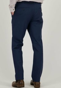 Marineblauwe broek van gestructureerde stof, met een recht model, twee achterzakken met knopen, gedragen met bruin schoenen.