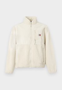 Cremefarget fleecejakke med glidelås i front, høy krage og strukturert kropp; har et lite logo-patch og to sidelommer.