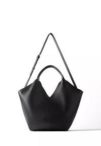Sac à main en cuir noir avec une forme structurée, des poignées courtes et une longue bandoulière réglable sur fond blanc.