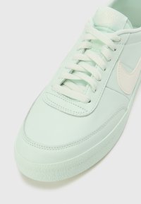 Baskets Nike en cuir vert menthe clair avec des lacets ton sur ton, une semelle en caoutchouc texturée et un logo swoosh beige subtil sur le côté.