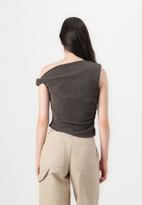 Brown textured crop top with an off-shoulder design, featuring rolled sleeves and a fitted silhouette, paired with beige wide-leg pants.