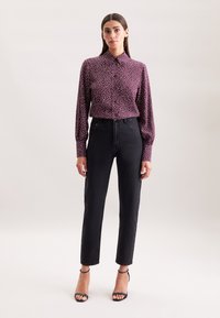 Bordeaux knoop-overhemd met witte stippen; lange mouwen; gecombineerd met hoge zwarte jeans en zwarte bandjeshakken.