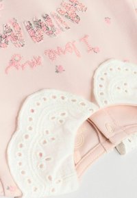 Rosa Babystrampler mit floralem Stickerei und Spitzenakzenten. Verfügt über Druckknöpfe für den Verschluss und einen weichen, strukturierten Stoff.