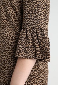 Tissu à imprimé léopard avec une coupe décontractée et un détail de manches à volants. Les couleurs comprennent le beige, le marron et le noir dans un motif texturé.