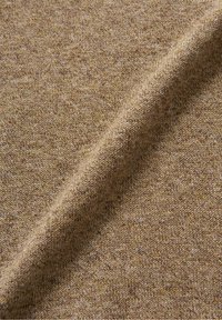 Stickad tyg i en varm, ljusbrun färg med ett texturerat mönster. Materialet visar en mjuk, lätt väv, som passar för lager på lager-kläder.