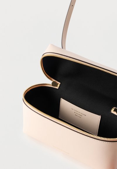 Μπεζ δερμάτινη τσάντα χειρός με χρυστό φερμουάρ, μαύρο εσωτερικό και ραμμένη ετικέτα που αναγράφει "Victoria Beckham, Made in Italy".