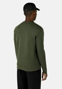 Olivgrön sweatshirt med bakvy, med rund hals och mjuk textur. Svart keps ger kontrast; liten logotypdetalj vid fållen.