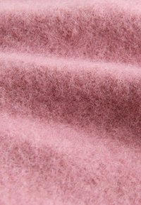 Tissu en feutre rose montrant une texture douce et duveteuse avec des plis ondulés, mettant en valeur son apparence chaleureuse et sa légèreté.