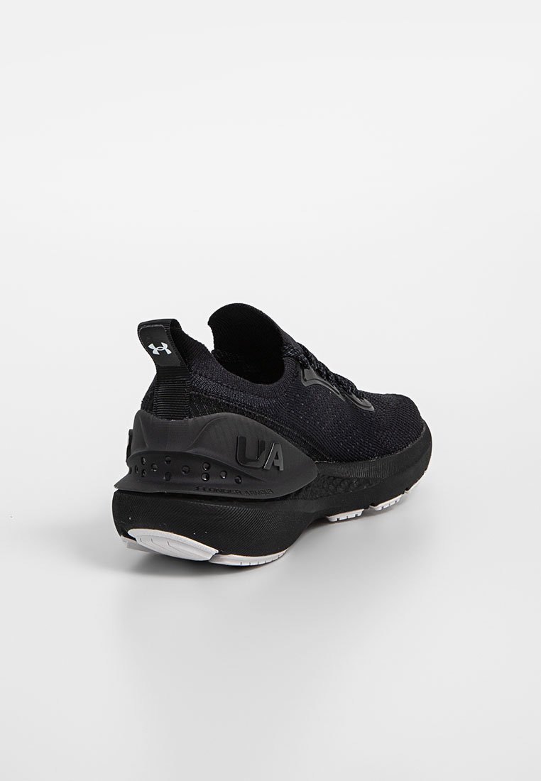 Zapatilla deportiva negra con un upper de punto texturizado, una suela acolchada en negro y blanco, y un logo UA prominente en el talón.