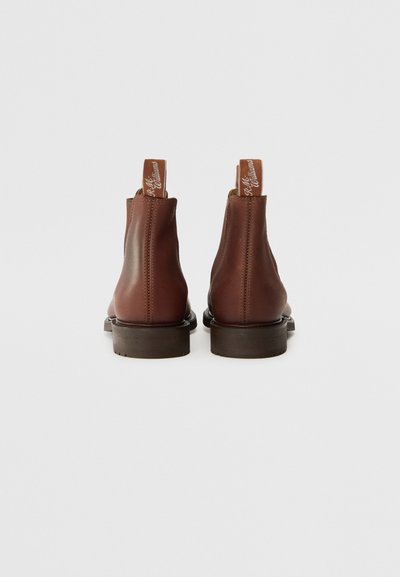 Bottines en cuir marron avec une texture lisse, présentant une couture et une semelle en caoutchouc marron, avec un logo sur l'anneau de tirage au talon.
