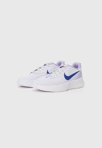 Baskets blanches de sport avec un matériau texturé, présentant un accent violet et un swoosh Nike bleu. Semelle blanche épaisse avec un motif de semelle.