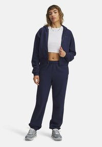Súprava navy blue mikiny a teplákov, vyrobená z mäkkého materiálu. Má zipsový predný diel, elastický pás a logo na oboch kusoch.