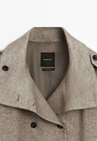 Beige dobbeltradet frakke med brede revers, sorte knapper og Massimo Dutti-mærke indeni kraven, lavet i Rumænien.