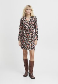 Robe portefeuille florale noire, ornée d'un mélange de motifs rouges, blancs et jaunes. Manches longues et taille cintrée, complétée par des bottes marron jusqu'au genou.