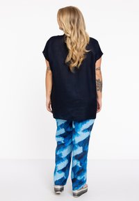 Marineblauw losvallend topje, gecombineerd met blauwe met patronen bedekte broek met zigzag ontwerpen. Het materiaal lijkt zacht met een ontspannen silhouet.