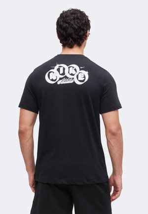 Homme de dos portant un t-shirt noir Nike avec un logo blanc « Nike Athletics » centré sur le haut du dos sur un fond uni.