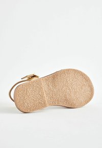 Sandalen mit einer strukturierten beigen Sohle, die ein flaches Design und einen Riemen mit goldfarbener Schnalle aufweisen. Die Sohle hat eine leicht erhöhte, griffige Textur.