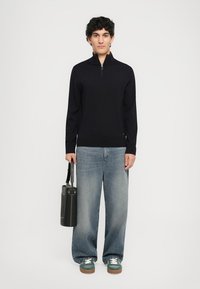 Mörkblå zip-up tröja, ribbade muddar och fåll, kombinerad med ljusblå vida jeans. Svart cylindrisk väska och gröna sneakers med vita snörning.