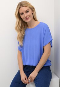 Top corto blu in un tessuto leggero con una vestibilità rilassata e una texture a coste, abbinato a jeans in denim blu scuro.