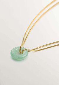 Collar de cadena de oro con un colgante de dona de piedra verde translúcida, de textura suave y acabado pulido.