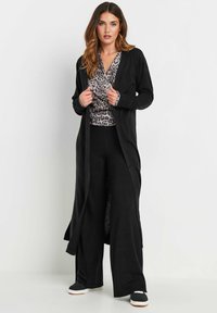 Svart lång cardigan med öppen front, tillsammans med en grå leopardmönstrad topp och svarta vida byxor. Har långa ärmar och mjuk textur.