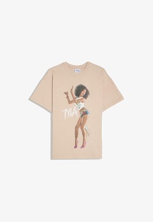 T-shirt beige avec un graphisme représentant une femme dansant, portant un short coloré, un haut blanc, des talons roses, avec le texte "TYLA" à côté d'elle.