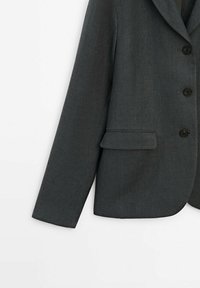 Blazer gris foncé sur mesure avec col cranté, trois boutons noirs et une poche à rabat sur le côté gauche avant.