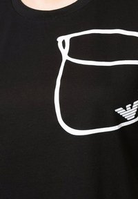 T-shirt nera in cotone con una linea bianca che delineata una tasca sul petto e un logo bianco con ali striate in basso a destra.