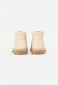 Beige suède enkellaarzen met een zachte kraag, rubberen zool en textuurhak. Het ontwerp heeft minimale stiksels en een ronde neus.