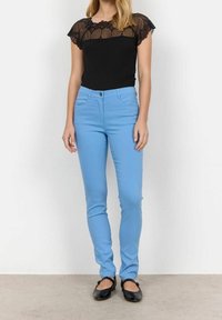 Zwarte kanten top met korte mouwen, gecombineerd met lichtblauwe nauwsluitende jeans en zwarte ballerina's. De top heeft een transparant kantontwerp bij de halslijn.