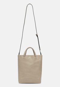 Sac fourre-tout en cuir beige avec deux poignées supérieures et une longue sangle noire réglable. Texture lisse, design minimaliste et logo discret à la base.