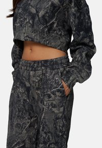Afgeknotte, donkergrijze sweatshirt en bijpassende joggers met een getextureerd camouflagepatroon. Beschikt over een elastische tailleband en zijzakken.