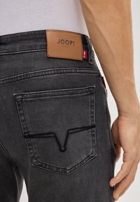 Ciemnoszare dżinsy ze skórzaną naszywką z logo "JOOP! JEANS" oraz kontrastowymi szwami kieszeni z tyłu w kształcie litery V.