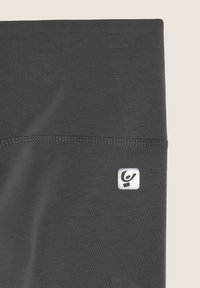 Leggings grigi scuri realizzati in un tessuto elasticizzato, con una cucitura e un piccolo logo argentato sul lato sinistro in basso.