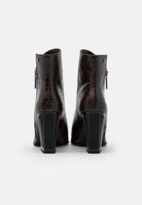 Botas de tobillo de cuero sintético en color marrón con relieve de cocodrilo, diseño elegante, tacones cuadrados y detalle de cremallera lateral. Acabado texturizado con acentos brillantes.