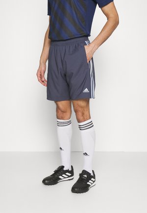 Donkerblauwe sportshorts met drie witte strepen, elastische tailleband en zijzakken, gecombineerd met kniehoge witte sokken en zwarte voetbalschoenen.