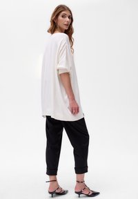 Witte oversized gebreide trui met geribde boorden, gecombineerd met zwarte broek met omslagen en zwarte hakken. Gladde textuur, licht kleurcontrast.