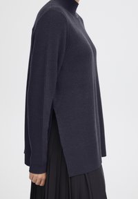 Navy-blauer Strickpullover mit hohem Kragen, gerippten Bündchen und Saum, seitlichen Schlitzen für Bewegungsfreiheit und einer strukturierten Oberfläche.