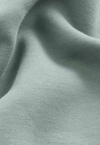 Tessuto a maglia verde chiaro con una fine texture a costine, caratterizzato da una superficie liscia che si drappeggia e piega dolcemente con una leggera lucentezza.