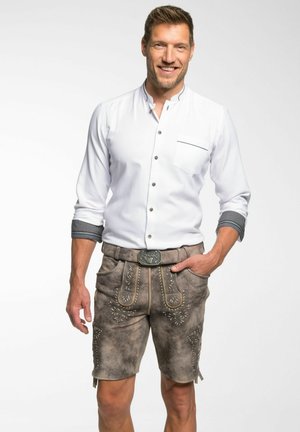Witte button-up shirt met een zak, gecombineerd met bruine lederhosen met decoratieve stiksels en een zilveren riemgesp.