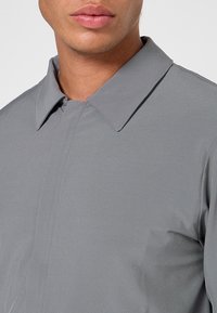 Grau meliertes Hemd mit glatter Textur; verfügt über eine Knopfleiste und eine taillierte Passform, die klare Linien und minimalistisches Design betont.