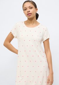 Κοντό φόρεμα σε ανοιχτό κρεμ με ροζ καρδιές, ριμπ ύφασμα, στρογγυλή λαιμόκοψη και κυματιστά τελειώματα στα μανίκια.