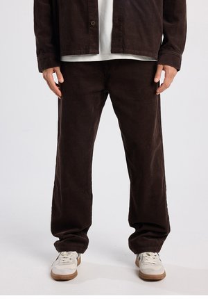 Braunes Cordjacken- und Hosen-Set mit geripptem Muster; lockere Passform; kombiniert mit weißem T-Shirt und hellen Sneakern.