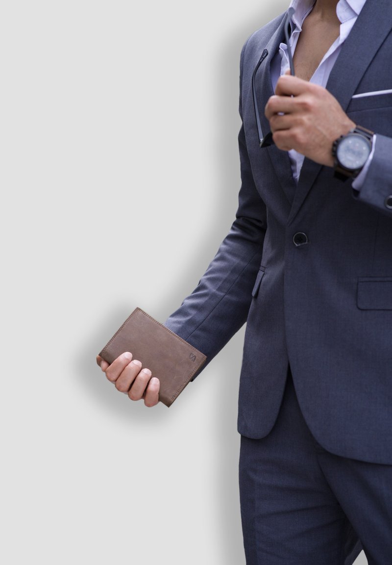 Brown leather wallet held in a hand, featuring a smooth texture and subtle stitching, against a backdrop of a gray suit jacket.