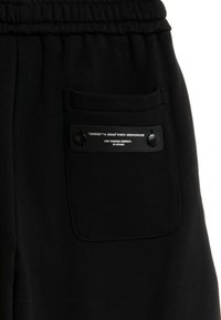 Los pantalones de chándal negros cuentan con una cintura con cordón, un bolsillo trasero con una etiqueta metálica y una tela de textura suave.