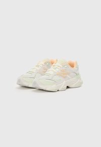 Baskets blanches avec des accents pastel vert et pêche, tige en mesh et synthétique, semelle épaisse, détails texturés et logo proéminent sur le côté.